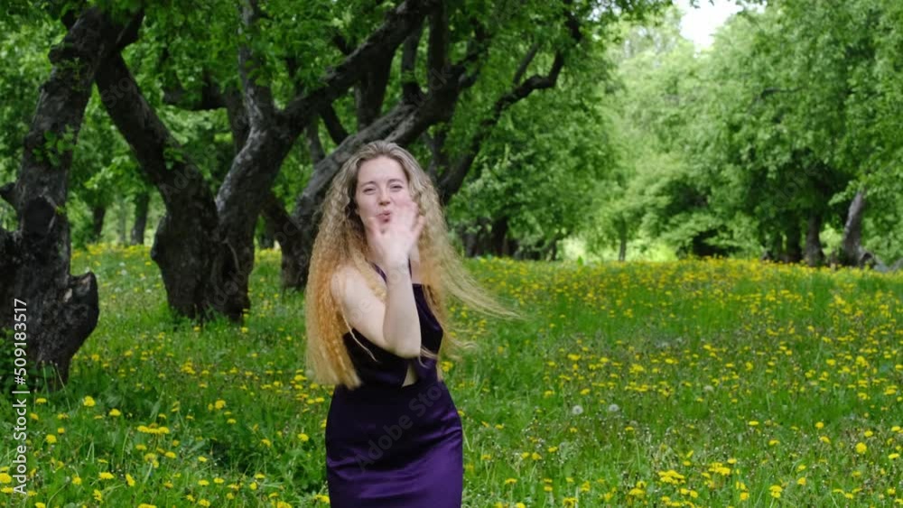 a cheerful, slender woman with long hair and a dress whirls on green grass with blooming dandelions in an apple orchard a cheerful, slender woman with long hair and a dress whirls on green grass with blooming dandelions in an apple orchard