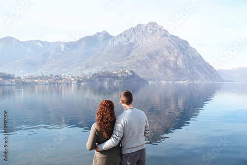 Soft focus, back view of couple embracing each other on the shores of Lake Lecco, Italy. People in love on a background of mountains and water outdoors enjoy a date. Romantic relationship. Copy Space