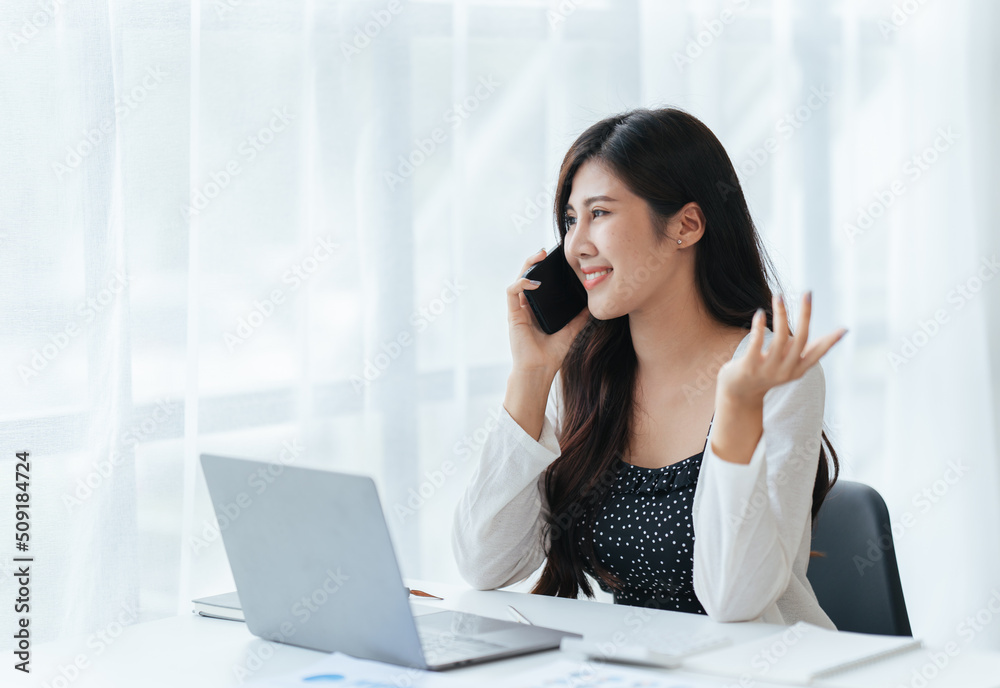 Cheerful young beautiful woman talking on mobile phone and using laptop with smile while sitting at her working place. Cheerful young beautiful woman talking on mobile phone and using laptop with smile while sitting at her working place.