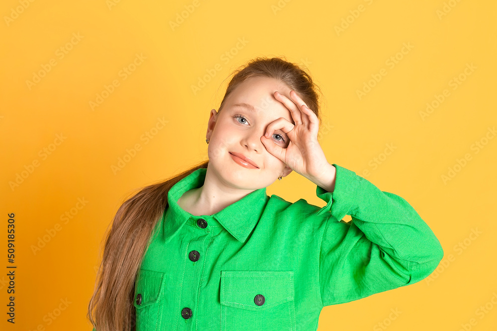 Portrait of a beautiful smiling little girl with long hair. A girl in a green suit on a yellow background in the studio shows emotions. place for text Portrait of a beautiful smiling little girl with long hair. A girl in a green suit on a yellow background in the studio shows emotions. place for text