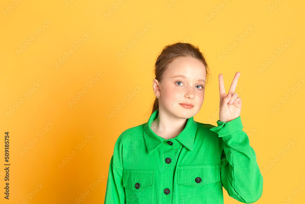 Portrait of a beautiful smiling little girl with long hair. A girl in a green suit on a yellow background in the studio shows emotions. place for text Portrait of a beautiful smiling little girl with long hair. A girl in a green suit on a yellow background in the studio shows emotions. place for text