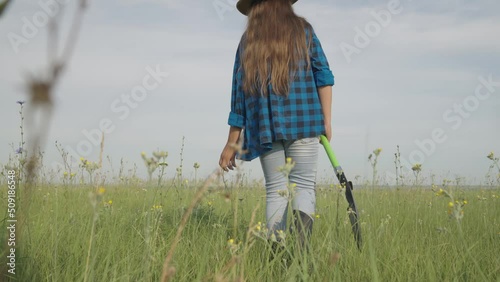 Girl strolls in field grass holding shovel against nasty sky photo