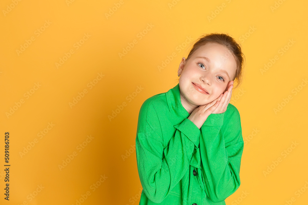 Portrait of a beautiful smiling little girl with long hair. A girl in a green suit on a yellow background in the studio shows emotions. place for text Portrait of a beautiful smiling little girl with long hair. A girl in a green suit on a yellow background in the studio shows emotions. place for text