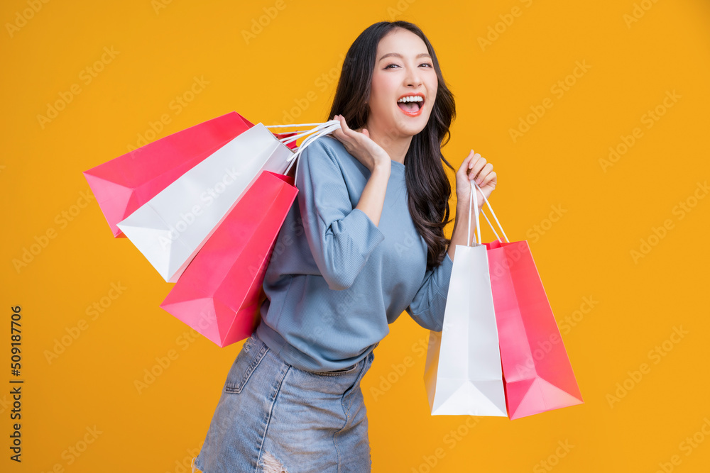 Asian happy female woman girl holds colourful shopping packages standing on yellow background studio shot, Close up Portrait young beautiful attractive girl smiling looking at camera with bags Asian happy female woman girl holds colourful shopping packages standing on yellow background studio shot, Close up Portrait young beautiful attractive girl smiling looking at camera with bags