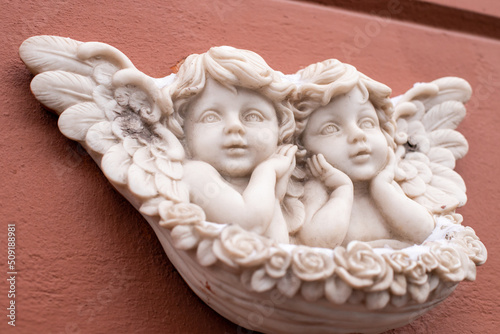 Two baby angels with wings marble sculpture on red wall of building. Close-up, front view. © Анастасия Бурлакова
