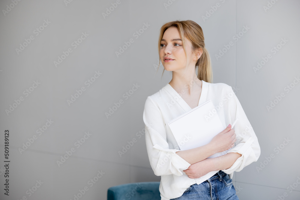 Fototapeta premium Young blonde woman in blouse holding notebook at home.