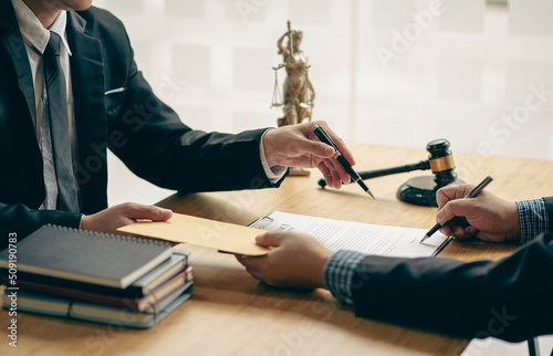 Businessman and lawyer man discussing legal matters and signing contract papers with judge's hammer with the goddess of justice in a team meeting at Law Concepts Office background and services.
