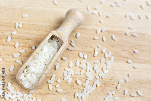 Dry grains of white round rice in a scoop on a wooden background. Space for text.