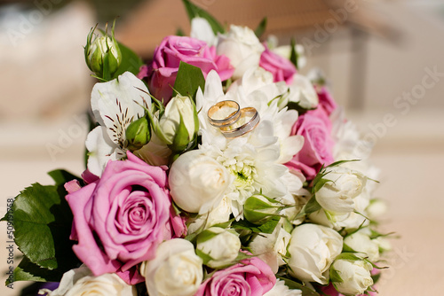 Composition with the bride s bouquet of pink roses and wedding rings visible from a high angle.