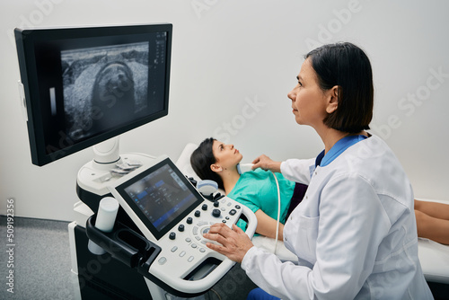 Endocrinologist making ultrasonography to female patient at ultrasound office of medical clinic. Ultrasound diagnostics of thyroid gland photo