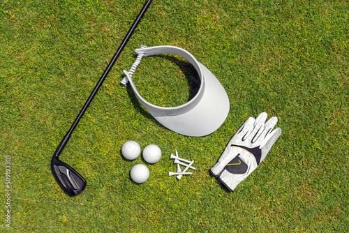 Top view of golf equipment on green grass on a golf course. Flat lay of golf club, balls, glove, tees and cap