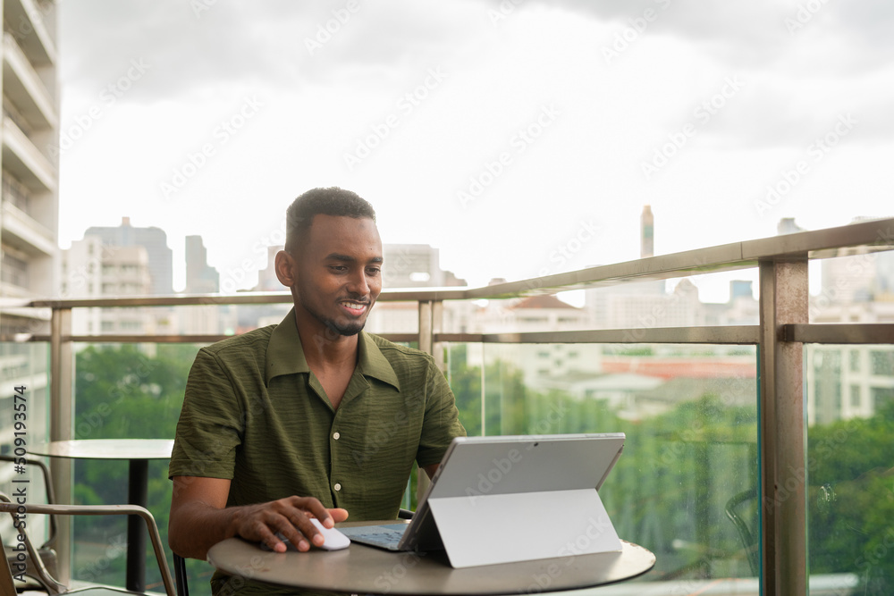 Handsome young black man using laptop computer in coffee shop outdoors
