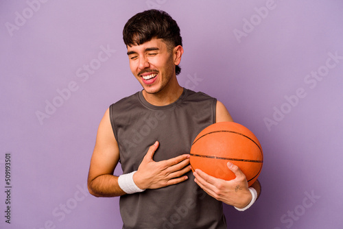 Young hispanic basketball player man isolated on purple background laughing and having fun. © Asier