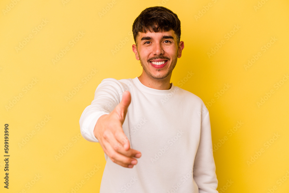 Young caucasian man isolated on yellow background stretching hand at camera in greeting gesture. Young caucasian man isolated on yellow background stretching hand at camera in greeting gesture.