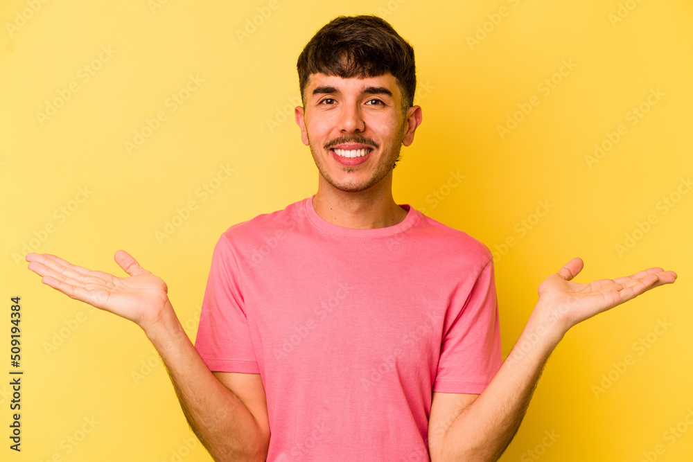 Young caucasian man isolated on yellow background makes scale with arms, feels happy and confident. Young caucasian man isolated on yellow background makes scale with arms, feels happy and confident.