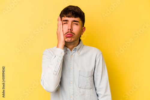 Young caucasian man isolated on yellow background tired and very sleepy keeping hand on head.
