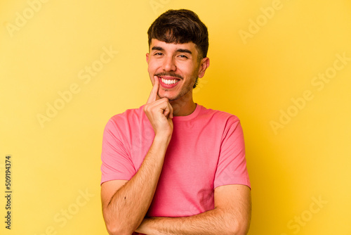 Young caucasian man isolated on yellow background smiling happy and confident, touching chin with hand.