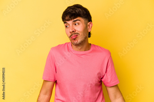 Young caucasian man isolated on yellow background shrugs shoulders and open eyes confused.