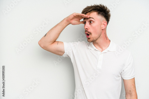 Young caucasian man isolated on white background looking far away keeping hand on forehead.