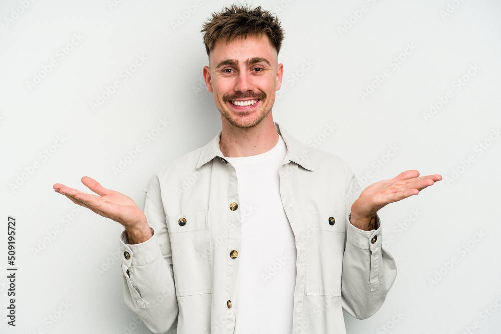 Young caucasian man isolated on white background makes scale with arms, feels happy and confident.
