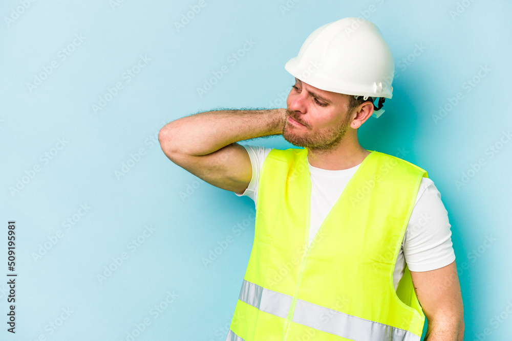 Young laborer caucasian man isolated on blue background touching back of head, thinking and making a choice.