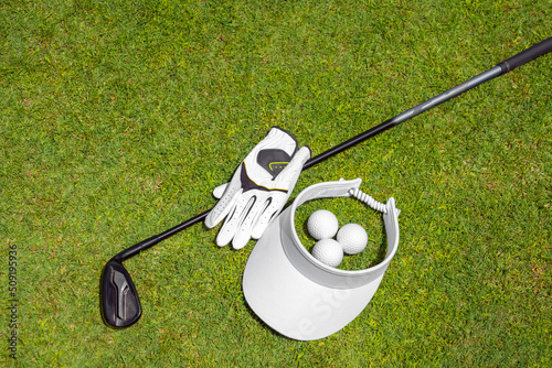 Top view of golf equipment on green grass on a golf course. Flat lay of golf club, balls, glove and cap