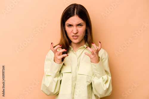 Young hispanic woman isolated on beige background upset screaming with tense hands.