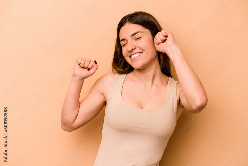 Young hispanic woman isolated on beige background celebrating a special day, jumps and raise arms with energy.