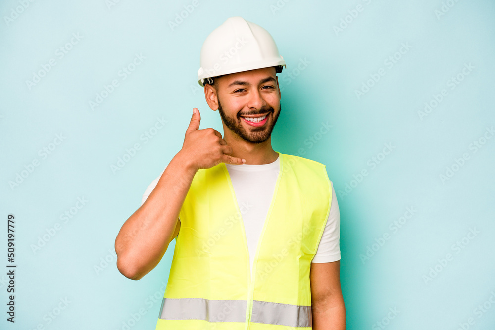 Young laborer hispanic man isolated on blue background showing a mobile phone call gesture with fingers.