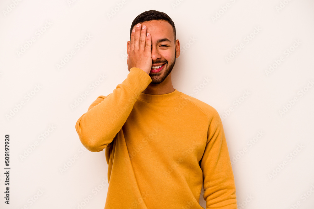 Young hispanic man isolated on white background having fun covering half of face with palm.