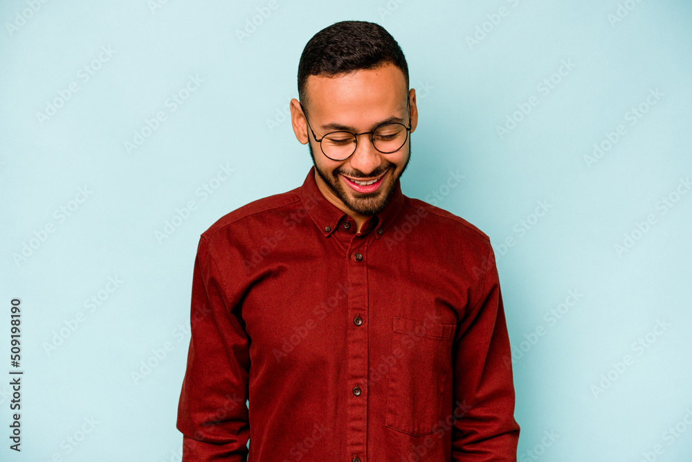 Obraz premium Young hispanic man isolated on blue background laughs and closes eyes, feels relaxed and happy.