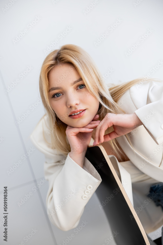 Young woman in jacket looking at camera near chair in living room. Young woman in jacket looking at camera near chair in living room.