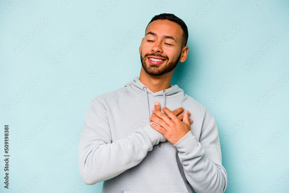 Young hispanic man isolated on blue background has friendly expression, pressing palm to chest. Love concept. Young hispanic man isolated on blue background has friendly expression, pressing palm to chest. Love concept.