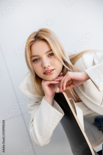 Young woman in jacket looking at camera near chair in living room.