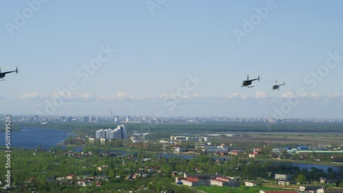 A three Robinson helicopters flies against background of river and cityscape. A group of helicopters flies against the blue sky on a sunny summer day. Film grain texture. Pixel texture. photo