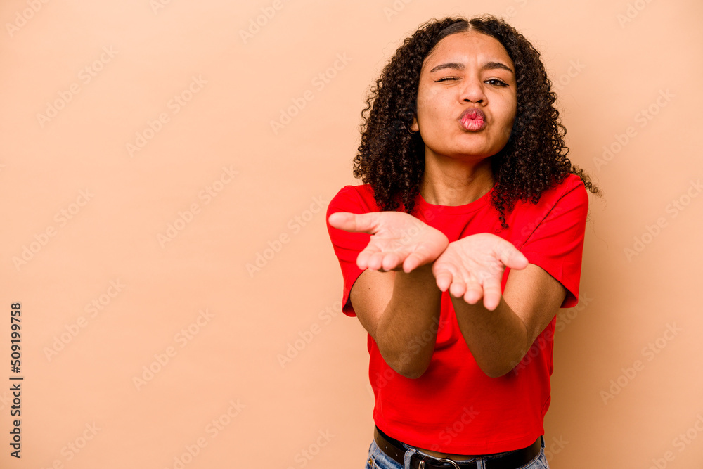 Young African American woman isolated on beige background folding lips and holding palms to send air kiss. Young African American woman isolated on beige background folding lips and holding palms to send air kiss.