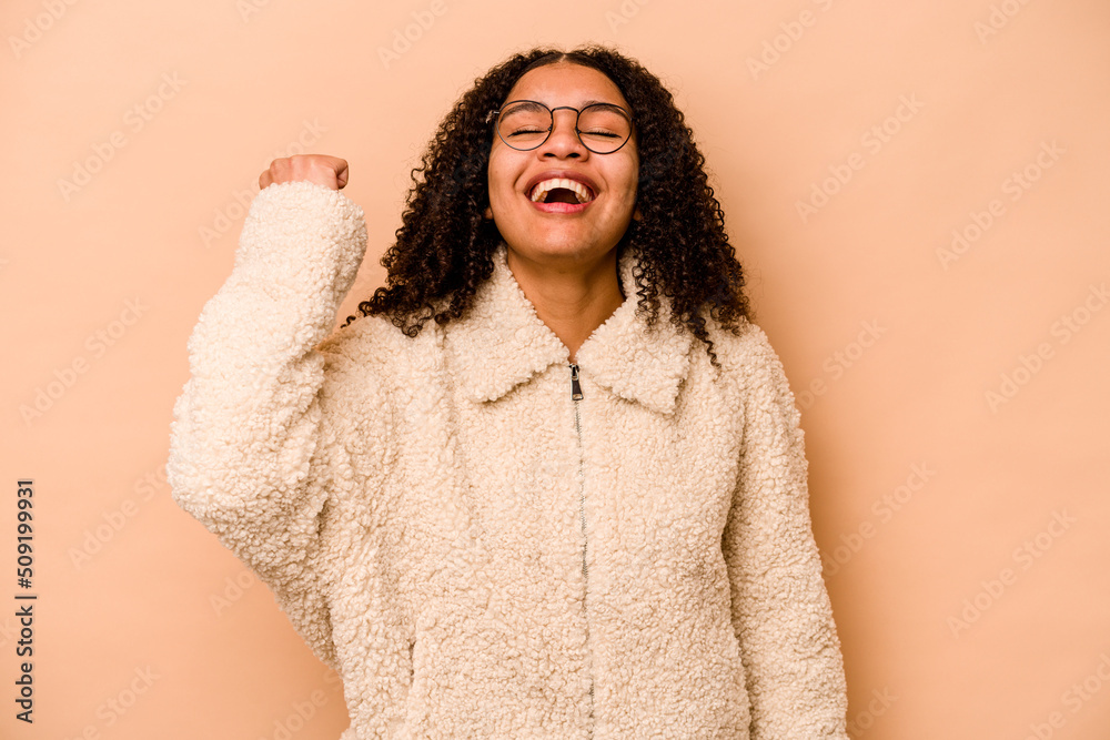 Young African American woman isolated on beige background celebrating a victory, passion and enthusiasm, happy expression.