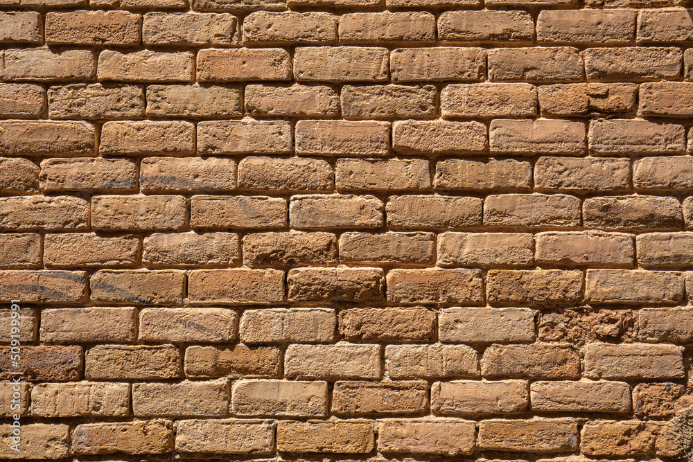 Reddish brown rectangular clay brick wall of an old house creating a geometric texture of lines and rows of elements