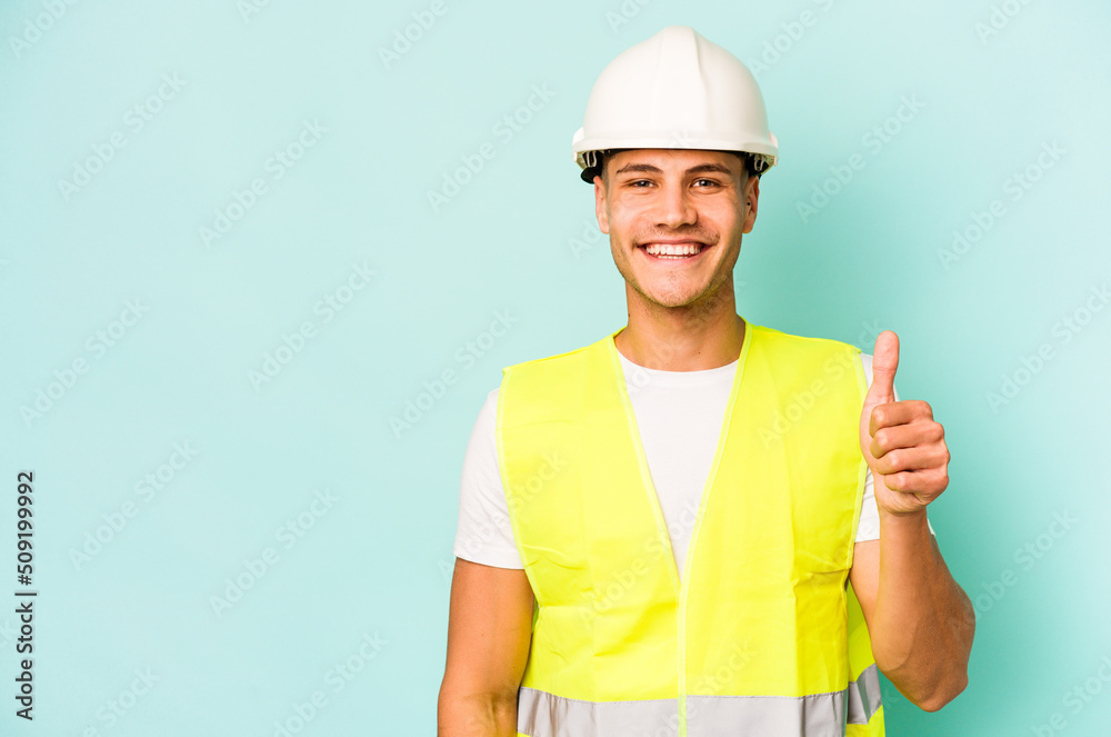 Young laborer caucasian man isolated on blue background smiling and raising thumb up