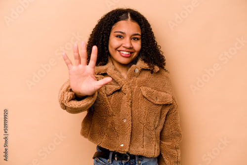 Young African American woman isolated on beige background smiling cheerful showing number five with fingers.