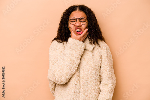 Young African American woman isolated on beige background having a strong teeth pain, molar ache. © Asier