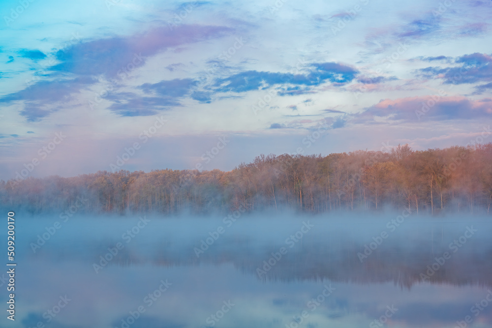 Foggy spring landscape at dawn of the shoreline of Deep Lake with mirrored reflections in calm water, Yankee Springs State Park, Michigan, USA
