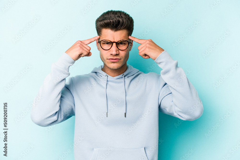 Young caucasian man isolated on blue background focused on a task, keeping forefingers pointing head.