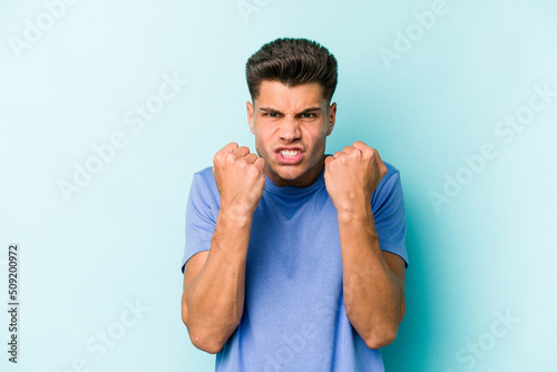 Young caucasian man isolated on blue background showing fist to camera, aggressive facial expression. © Asier
