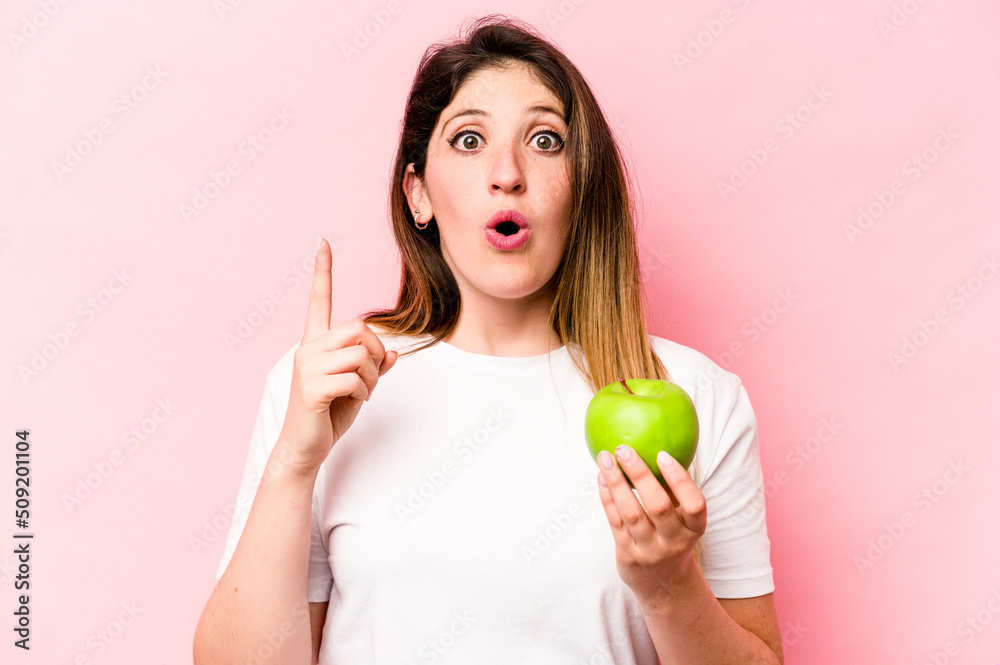 Young caucasian woman holding an apple isolated on pink background having some great idea, concept of creativity. Young caucasian woman holding an apple isolated on pink background having some great idea, concept of creativity.