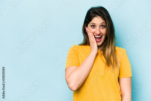 Young caucasian woman isolated on blue background shouts loud, keeps eyes opened and hands tense.