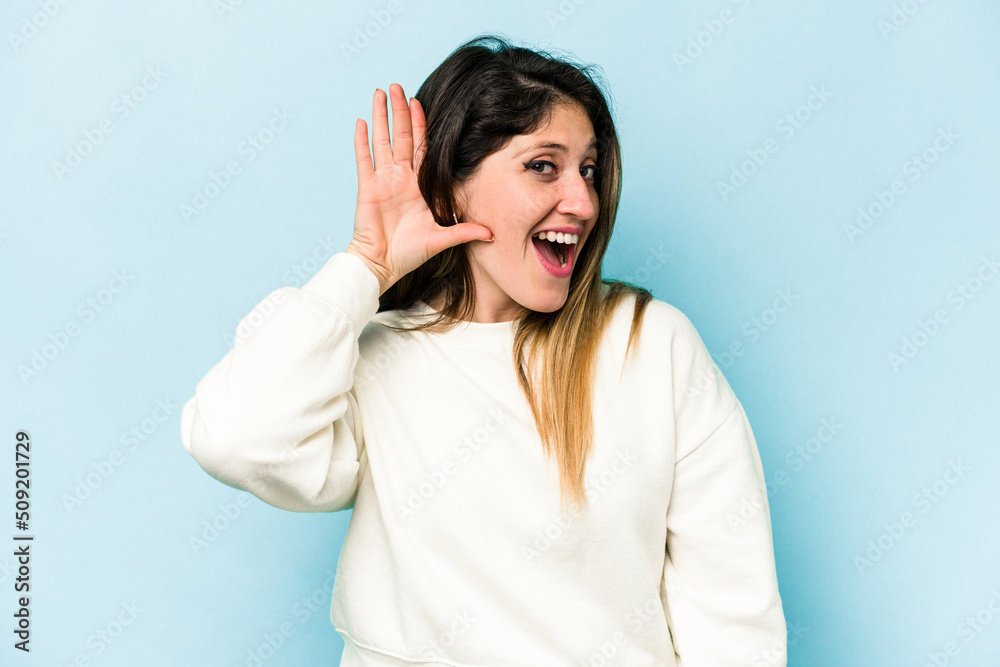 Young caucasian woman isolated on blue background trying to listening a gossip. Young caucasian woman isolated on blue background trying to listening a gossip.