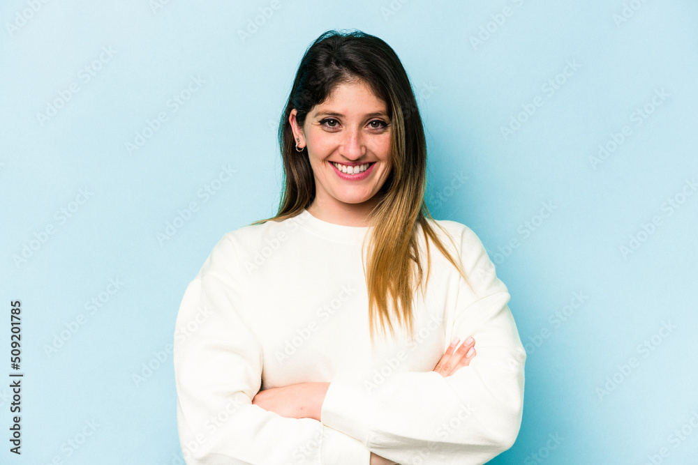 Young caucasian woman isolated on blue background who feels confident, crossing arms with determination. Young caucasian woman isolated on blue background who feels confident, crossing arms with determination.