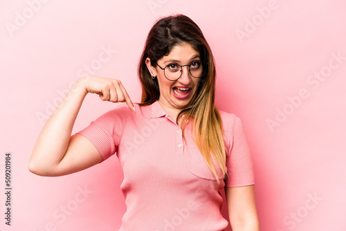 Young caucasian woman isolated on pink background person pointing by hand to a shirt copy space, proud and confident