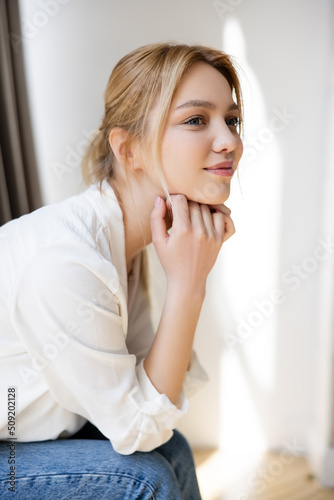 Pretty young woman in blouse looking away at home.